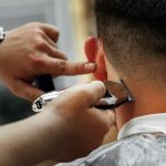Barber guy gives a haircut to a bearded man sitting in a chair in a barbershop